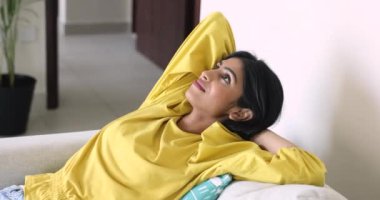 Mutlu genç 20 'li yaşlarda rahat bir kanepede dinlenen yumuşak sırtlı, kollarını başının altında tutan, gözlerini kapatan, uykuya dalan, temiz hava soluyan, rahatlayan, rahatlayan, konforlu bir kız.