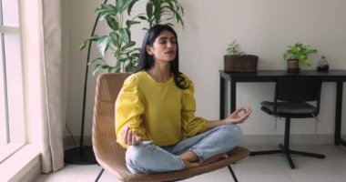 Huzurlu genç Hintli kadın derin nefes alarak meditasyon yapıyor, koltuğunda oturmuş zen parmaklarıyla poz veriyor, t6ranquility uygulamasının tadını çıkarıyor, huzur, sakinlik, eğitim konsantrasyonu.