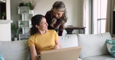 Mutlu, genç, İspanyol bir kız ve yaşlı bir anne, içinde sürpriz bir hediye olan karton bir lojistik kutuyu açıyor, evde paketleri açıyorlar, heyecanlanıyorlar, neşeliler.