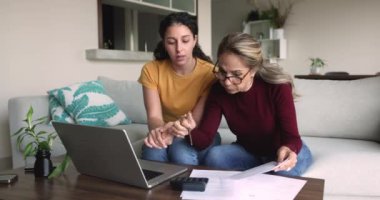 Yetişkin bir anne genç yetişkin kızına ev faturalarını ödemeyi öğretiyor, hesap makinesindeki kağıt faturalarını kontrol ediyor, bilgisayardaki finansal uygulamayı kullanıyor, yetişkin bir çocuğa beşlik çakıyor.