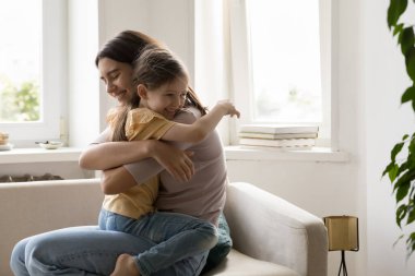 Küçük güzel kız, kucağına oturup anne kucağına oturuyor sevgi duyuyor, aile kucaklıyor, şefkat ve özen gösteriyor, birlikte oturma odasında vakit geçiriyorlar. Koşulsuz sevgi, sıcaklık, ilişkiler, bağlar.