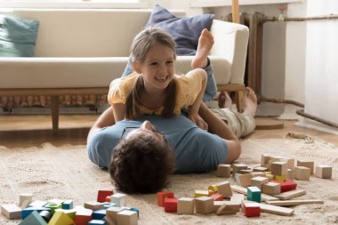 Neşeli küçük kız, sevgi dolu babasıyla oturma odasında oynuyor, aile yerde yatıyor, eğleniyor, evde kaygısızca vakit geçiriyor, gıdıklanıyor, gülüyor, mutlu oluyor. Babalık, bağlar ve bağ