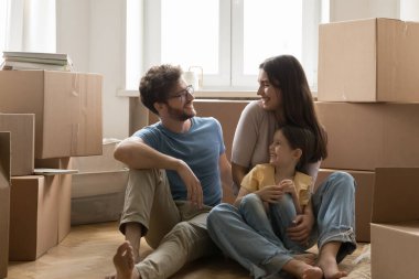 Kızıyla mutlu bir aile yeni evi satın almayı kutluyor oturma odasında yere oturduktan sonra rahatlıyor. Uzun vadeli kira, genç aile için banka ipoteği, uygun fiyatlı ev, yeni bir hayat.