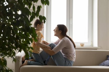 Sevgi dolu anne ve tatlı küçük kız evdeki kanepede oturur, eğlenir, birlikte keyifli ve sıcak vakit geçirirsiniz. Genç aile oturma odasında vakit geçirir, sevgiyi hisseder, şefkati ifade eder. Annelik