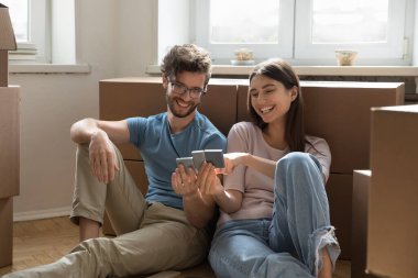 Mutlu genç çift yerde bir yığın karton kutuyla oturuyor kişisel eşyalarıyla zemin yüzey örneklerini seçiyor, yeni ev dekorasyonu renklerini gözden geçiriyor, yenilemeyi planlıyor, iç tasarımı tartışıyorlar.