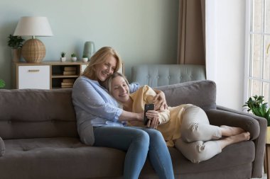 Neşeli, olgun bir anne, akıllı telefonlu güzel kızına sarılıyor, online medya içeriğini izliyor, video görüşmesi yapıyor, alışveriş yapıyor, internet iletişimi için cep telefonu kullanıyor.