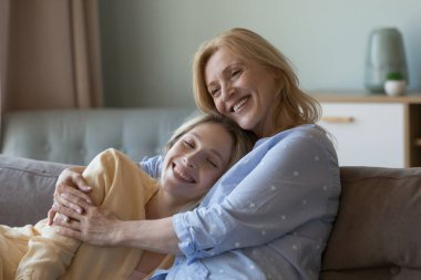 Mutlu yetişkin bir anne, sevgi, şefkat, minnettarlık, gülümseme, kahkaha, evde kanepede dinlenme anneliğin, aile toplantısının, boş zamanların, sıcak ilişkilerin keyfini çıkarıyor.