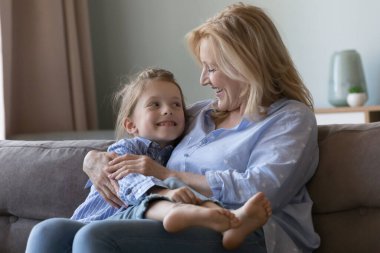 Olgun bir büyükanne kucağında küçük tatlı bir torun kızı kucağında, koltukta çocuğa sarılıyor, gülüyor, gülüyor, sevgi, şefkat, şefkat dolu bir çocukla konuşuyor, aile tatilinin tadını çıkarıyor.