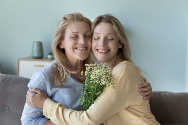 Neşeli yetişkin kız ve olgun anne 8 Mart 'ı kutluyor, anneler günü, elinde bahar çiçekleri, kanepede oturuyor, sevgiyle sarılıyorlar, sıcakkanlılıkla, şefkatle. Aile fotoğrafı.
