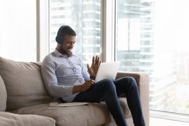 Kablosuz kulaklıklı neşeli yakışıklı girişimci bilgisayarın web kamerasına el sallıyor, merhaba diyor, gülümsüyor, iş arkadaşlarıyla konuşuyor, müşterilerle konuşuyor, evde çalışıyor.