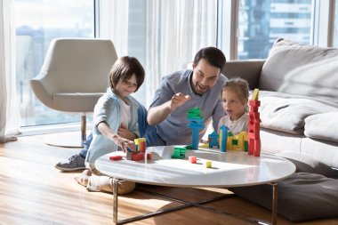 Heyecanlı neşeli baba iki küçük çocukla oyun oynayarak eğleniyor, çocuklarla oyuncak kulesini diziyor, oğul ve kızına kale inşa etmeyi öğretiyor, ebeveynliğin tadını çıkarıyor, hafta sonu,