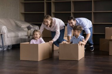 Heyecanlı mutlu ebeveynler ve çocuklar yeni eve taşınmayı kutluyorlar, yarışta yarışıyorlar, karton kutuları içeri taşıyorlar, bağırıyorlar, gülüyorlar, eğleniyorlar.