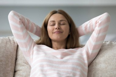 Huzurlu, mutlu, 30 'lu yaşlarda güzel bir kadın kanepeye uzanıyor, serin hava soluyor, meditasyon yapıyor, sakinliğini koruyor, tembelliğin tadını çıkarıyor, rahatlıyor, stres atma teknikleri uyguluyor.