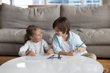 Neşeli küçük kardeş çocuklar yaratıcı hobilerini, boş zamanlarını, günlük aktivitelerini evde birlikte geçiriyorlar, sohbet ediyorlar, konuşuyorlar, kalemlerle çiziyorlar, renkli karalamaları tartışıyorlar.