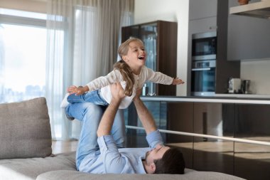 Neşeli heyecanlı şirin çocuklar babalarının kollarını ve bacaklarını dengede tutuyorlar, kollarını açıp uçan uçak oynuyorlar, gülüyorlar, bağırıyorlar, eğleniyorlar. Şefkatli baba babalığı seviyor, egzersiz yapıyor.