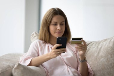 Milenyum güzeli müşteri kadını cep telefonunda ecommerce alışveriş uygulaması kullanıyor, kredi kartı kullanıyor, internet mağazasının internet sitesinden satın alma, evden satın alma, para transferi yapıyor.