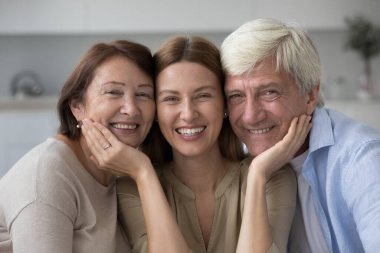 Mutlu yaşlı ebeveynler ve güzel yetişkin kız kız. Kafa teması ile yakın poz veren, dişlek gülümsemeli kameraya bakan, gülen, aile ilişkilerinden zevk alan, boş zaman, yakınlık.