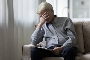 Depresyonda olan yaşlı bir adam kağıt belgelerden kötü haberler alıyor, evdeki kanepede oturuyor, yüzünü örtüyor, tıbbi sonuçlarla ilgili bilgiler alıyor, iflas uyarısı alıyor.