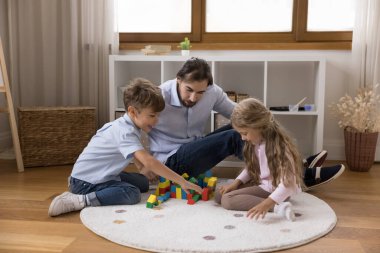 Babam küçük çocuklara bina, kule, oyuncak tahta bloklardan kale modeli renkli küpler ve tuğlalar yapmayı öğretiyor. Kreş öğretmeni ve çocuklar oyun odasındaki ısıtma katında öğrenme oyunu oynuyorlar