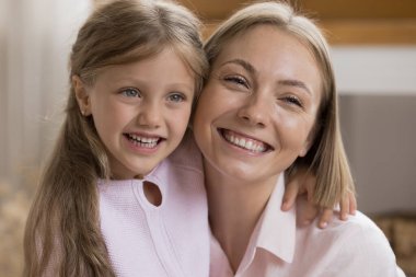 Güzel genç bir kadın ve küçük tatlı sarışın bir kız kucaklaşıp yan yana bakıyorlar. Kapalı alanda geniş dişli bir gülümseme takınarak portre çekiyorlar. Yaşam değeri, genç nesil, mutlu annelik kavramı.