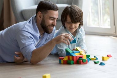 Mutlu baba meraklı çocuğa oyuncak tahmini yapmayı öğretiyor, kale, renkli bloklardan kule modeli, ısıtma tabanında çocukla öğrenme oyunları oynuyor. Babalık, aile kavramı