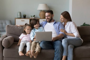 Mutlu aile çifti ve sevimli neşeli çocuklar evdeki koltukta dizüstü bilgisayar kullanıyorlar oturma odasında dinleniyorlar interaktif uygulama ve internet servisi ile film izliyorlar. Yurtiçi iletişim kavramı
