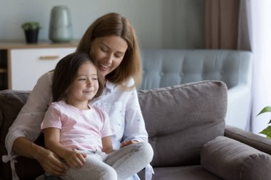 Neşeli bir anne koltukta kucağında küçük mutlu bir kız çocuğu kucağında, sevgi dolu, özenli, düşünceli hayalperest bir kızla konuşuyor, başka tarafa bakıyor. Annelik, aile eğlencesi konsepti