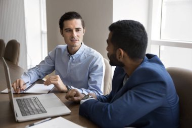 İki ciddi çok ırklı iş adamı dizüstü bilgisayar başında konuşuyor, online modern teknolojiyi takım çalışması, iletişim, internet girişimi, işbirliği stratejisi, toplantı masasında oturmak için kullanıyorlar.