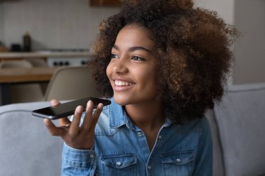 Hayalperest genç Afrikalı kız cep telefonuyla konuşuyor, sesli mesaj kaydediyor, sanal asistana sesli komut veriyor, düşünceli bir gülümsemeyle başka yere bakıyor.