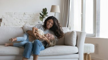 Neşeli, mutlu bir anne, kanepede sevimli küçük kızına sarılıyor, gıdıklıyor, kucaklıyor, kahkahalarla gülen çocuğu sevgiyle kucaklıyor. Anne aktiviteden zevk alıyor, evde oyun oynayan bir kızla vakit geçiriyor. Pankart