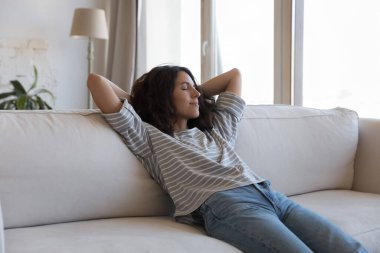 Sakin, güzel, uykulu, İspanyol bir kadın yumuşak kanepeye uzanıyor, arkasını yaslıyor, temiz hava soluyor, rahatlıyor, keyif alıyor, meditasyon yapıyor, evde kapalı gözlerle stres atağı yapıyor.