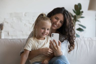 Mutlu anne kucağında küçük tatlı bir kız çocuğu, evde akıllı telefon kullanıyor, video konuşmaları yapıyor, selfie çekiyor. Blogcu anne çocuğa sevgi, şefkat ve cep telefonu kamerasıyla sarılıyor.