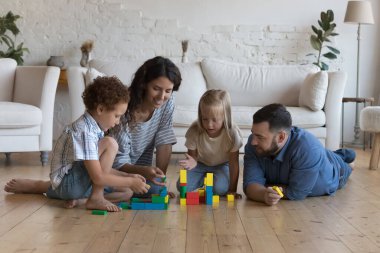 Mutlu ebeveynler ve küçük evlatlık çocuklar ısıtma tabanında birlikte oynuyorlar, ahşap oyuncak bloklarından kuleler inşa ediyorlar, çocukları öğrenme oyununda eğitiyorlar, aile eğlencelerinden, oyun zamanlarından keyif alıyorlar.