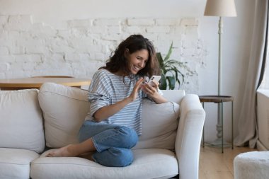 Heyecanlı, mutlu, genç bir kadın cep telefonundan mesaj okuyor, ekrandan iyi haberler alıyor, gülümsüyor, gülüyor, video görüşmeleri yapıyor, internette sohbet ediyor, online uygulama kullanıyor. İletişim konsepti