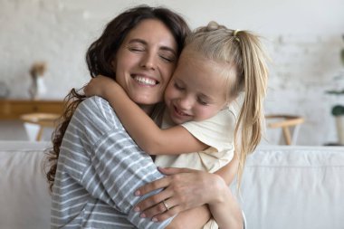 Sevgi dolu bir anne, mutlu, küçük kızına yanak yanağa sarılıyor. Anne portresi, kapalı gözlü, sevgi ve bağlılık gösteren bir kız çocuğu. Aile, ebeveynlik, annelik kavramı.