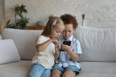 Cep telefonunda online uygulama kullanan, arama yapan, içeriği izleyen, internette gezinen, video oyunu oynayan, evde tek başına oturan iki sevimli Z-kardeş çocuk.
