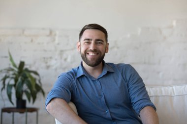 Evdeki kanepede oturan mutlu yakışıklı adam dişlek gülüşüyle kameraya bakıyor. Neşeli kendine güvenen blogcu çevrimiçi eğitim konferansı veriyor. Video çağrısı portresi