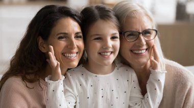 Çok nesilli akrabalar aile gününü kutluyor, poz veriyor, yana bakıyor, tatlı küçük kız yanaklarına dokunuyor mutlu yaşlı büyükanne ve genç annenin, yüzlerini kapatıyorlar portrelere bakıyorlar. Bağlar, aşk, bağlantı