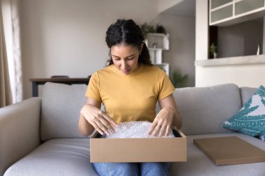 Genç İspanyol tüketicinin internet mağazasından gelen paketleri açması, kucağında plastik ambalajlı karton lojistik kutular, paketlerin açılması, paketin evde açılması.