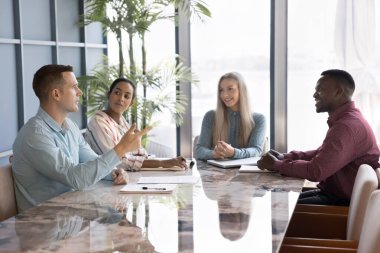 Ciddi başarılı iş adamı çeşitli meslektaşlarına proje için yaratıcı fikirleri açıklıyor. Çok ırklı bir ekip masada beyin fırtınası yapıyor, takım çalışmasını tartışıyor, gülümsüyor.