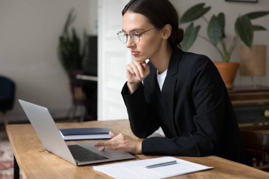 Dizüstü bilgisayarda çalışan ciddi odaklı bayan ofis çalışanı, edinilen bilgileri ya da belgeleri okuyun, meslektaşınızla iletişim kurun, müşterilerin veya hissedarların önerilerini gözden geçirin, idari işlerle ilgilenin