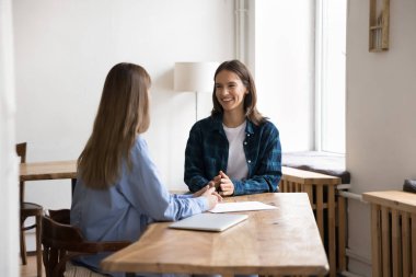 Modern ofis odasındaki çalışma masasında oturan ve ortak görev, proje veya konularla ilgili masa başı diyaloglarda oturan iki çekici genç bayan meslektaşı. İş görüşmesi süreci