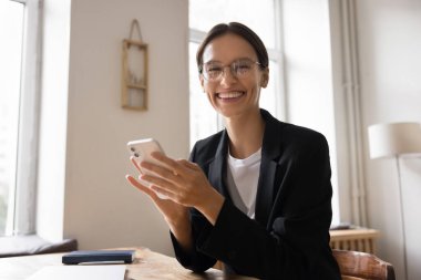 Mutlu iş kadını portresi, iş yerinde akıllı telefon kullanan ofis çalışanı, kameraya bakın, başarı, profesyonellik, e-posta ya da mesajla iyi haberler alın, iş gününün ve uzaktan iletişimin keyfini çıkarın.