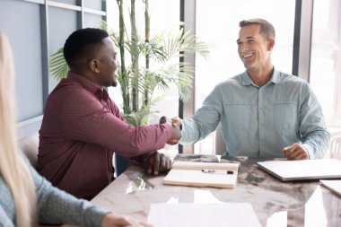 Mutlu, kendine güvenen bayan patron Afrikalı çalışanın elini sıkıyor, hoş geldin partneri, çalışanı, takım çalışması için teşekkür ediyor, ortaklık kuruyor, anlaşmayı bitiriyor, çalışanlara destek oluyor.