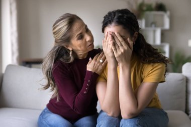 Sempatik yaşlı Latin anne, ağlayan genç kız kızı teselli ediyor, sinirli yetişkin çocuğa duygusal sorunlar için destek oluyor, evde oturan kızı kucaklıyor.