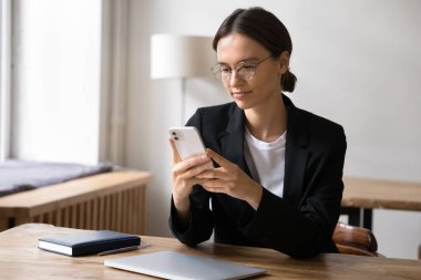 Çekici iş kadını akıllı telefonuyla işyeri masasında oturur, mobil bankacılık veya mali yönetim araçları kullanır, planlar, iş günlerini düzenler, iş ile ilgili sorunları uygulamayla verimli bir şekilde çözer