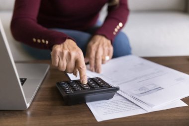 Evde hesap makinesi kullanan yaşlı bir kadının elleri kağıt belgeler okuyor, faturaları kontrol ediyor, faturaları ödüyor, vergi sayıyor emeklilik için tasarruf yapıyor, yatırım gelirleri artıyor. Yakın çekim kesilmiş.
