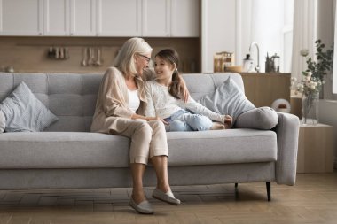 Küçük kız kanepede yaşlı bir büyükanneyle oturuyor, gülüyor, sohbetin tadını çıkarıyor, yakın, sevgi dolu bir ilişki ve sıcak paha biçilemez anlar. Rahatlık, bakım, mutluluk iki farklı nesil arasında paylaşılır.