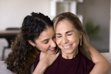 Mutlu genç kız kız, olgun İspanyol anneyi özenle, sevgiyle, sevgiyle kucaklıyor. Neşeli son sınıf öğrencisi Latin anne ve yetişkin çocuk kapalı gözlerle sarılıp gülüyorlar. Ev aile fotoğrafı.