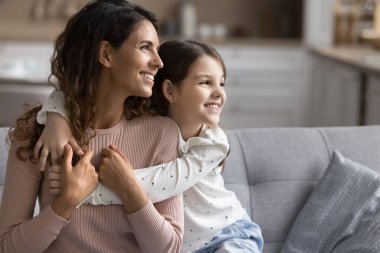 Anne ve kızı kanepede yan yana oturur ve başka tarafa bakarlar. Küçük kız, annesine arkadan şakayla sarılıyor sıcak ve sevecen bir anı paylaşıyor. Aile sevgisi ve birliktelik